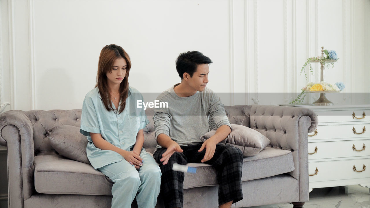 Sad couple throwing pregnancy test while sitting on sofa