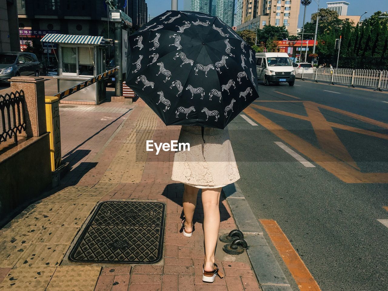 Rear view of woman holding umbrella while walking on sidewalk in city