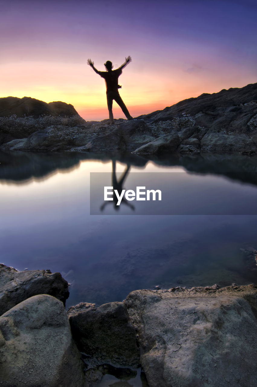 one person, reflection, rock, water, sky, adult, nature, sunset, silhouette, sea, beauty in nature, leisure activity, mountain, arm, tranquility, scenics - nature, full length, limb, tranquil scene, lifestyles, exercising, standing, balance, men, activity, arms raised, environment, human limb, holiday, vacation, idyllic, sports, relaxation, zen-like, land, dusk, trip, outdoors, cloud, yoga, arms outstretched, landscape, solitude, sun, spirituality, religion, vitality, darkness, evening, back lit, adventure, twilight, sunlight