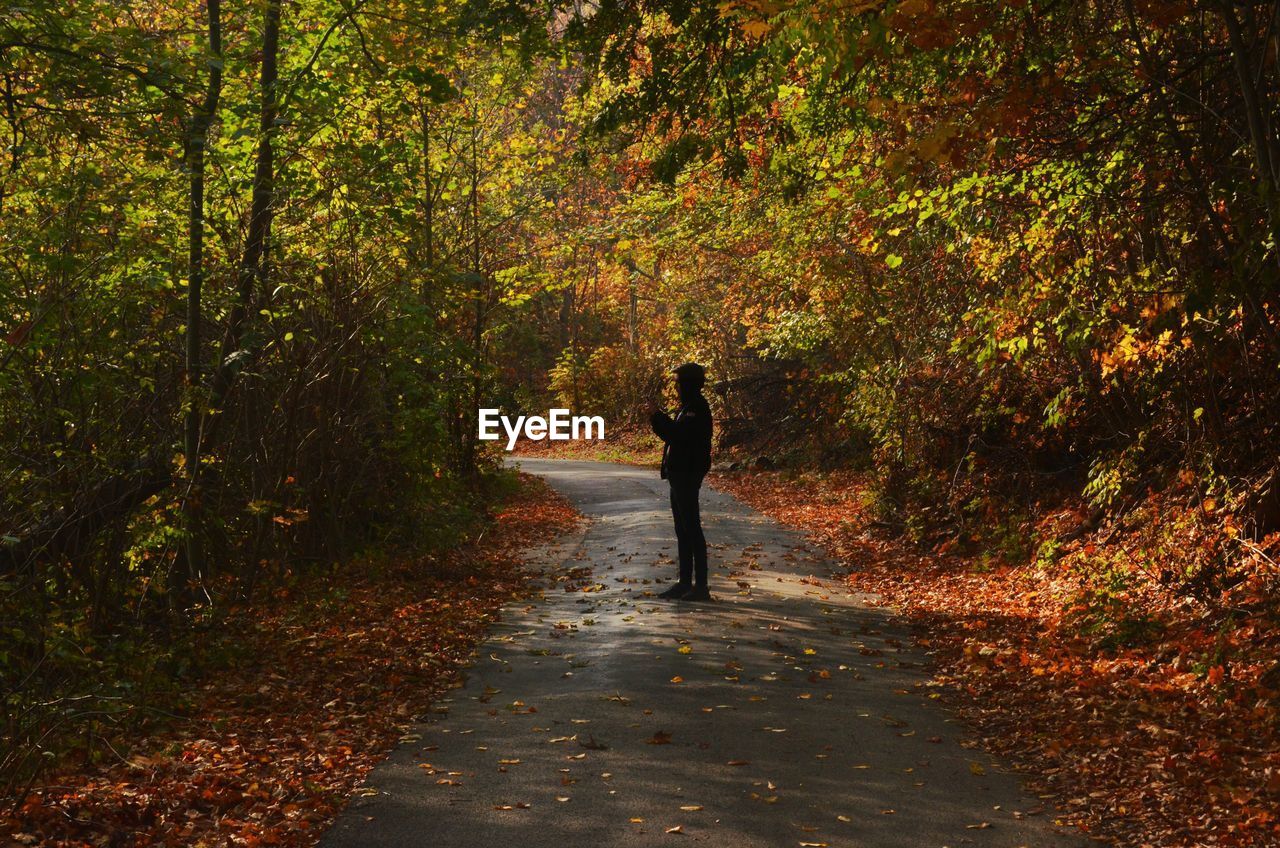 FULL LENGTH OF MAN STANDING AMIDST TREES IN FOREST DURING AUTUMN