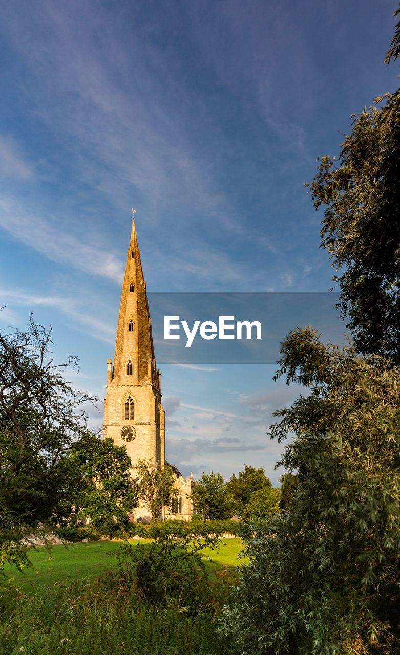 Low angle view of church clock tower amidst trees and buildings against sky