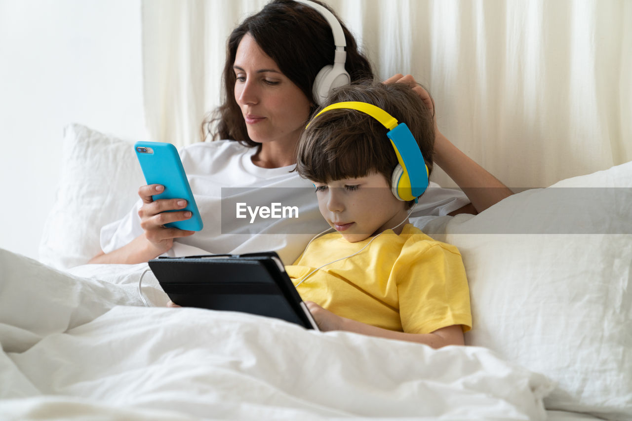 Mother and daughter using mobile and digital tab while relaxing on bed at home