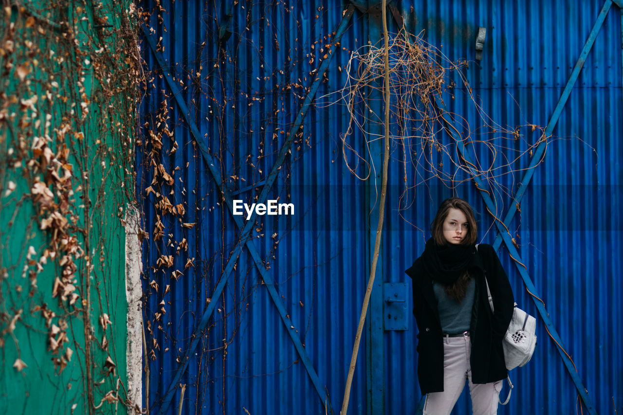 Portrait of young woman standing against blue corrugated iron