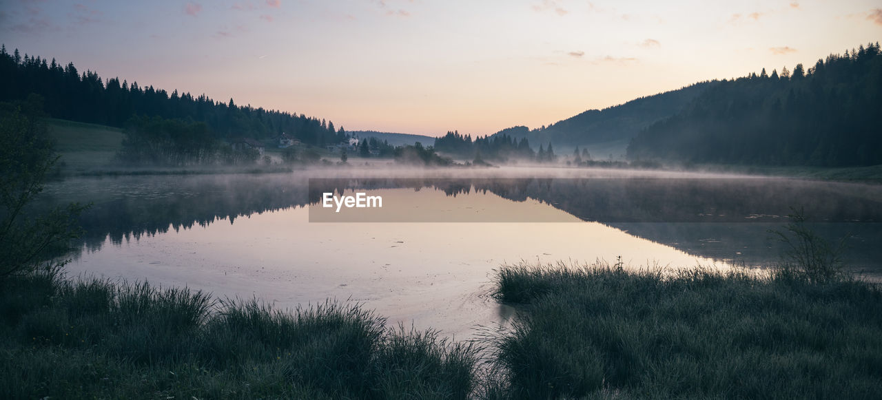 nature, reflection, water, morning, scenics - nature, plant, tree, beauty in nature, sky, lake, mist, tranquility, dawn, environment, landscape, tranquil scene, fog, forest, sunrise, land, mountain, no people, sun, wilderness, non-urban scene, twilight, reservoir, cloud, travel destinations, idyllic, pinaceae, outdoors, coniferous tree, pine tree, grass, body of water, pine woodland, woodland, travel, sunlight, tourism, rural scene