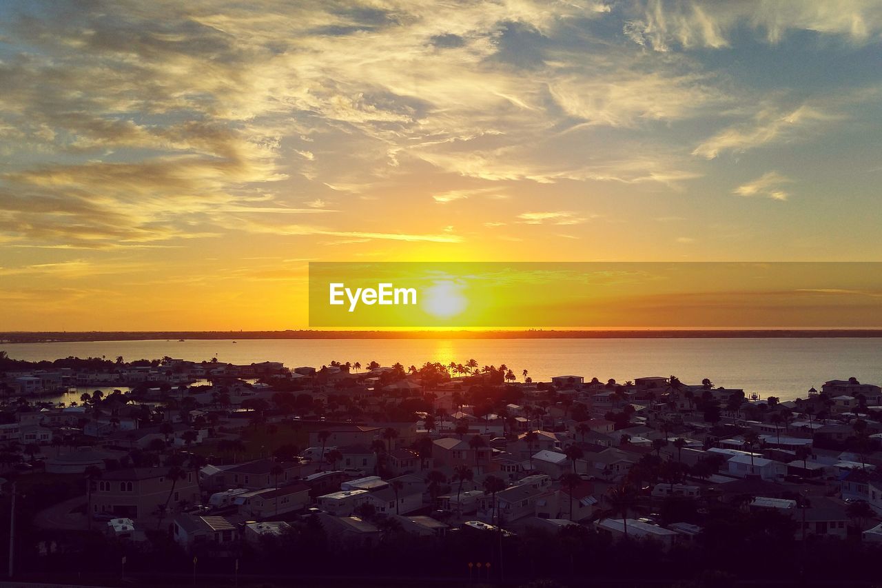 Scenic view of sea in front of buildings against cloudy sky during sunset