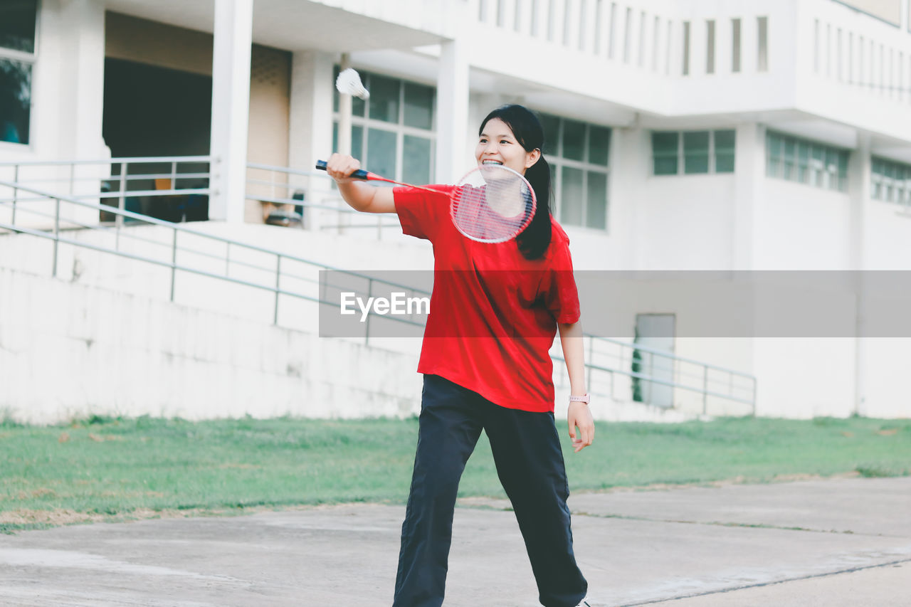 Smiling young woman playing badminton while standing outdoors