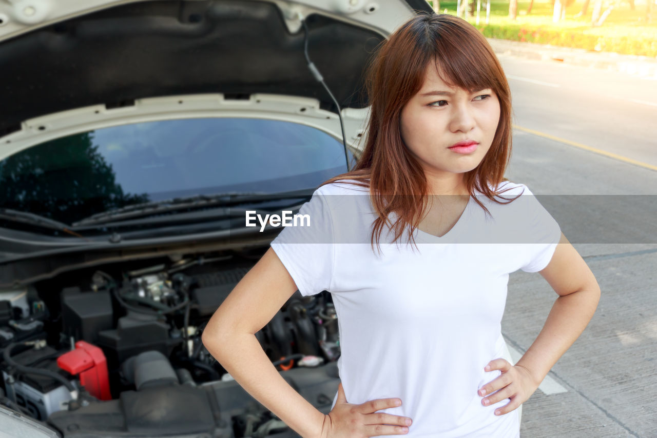 Woman looking away while standing by car on street