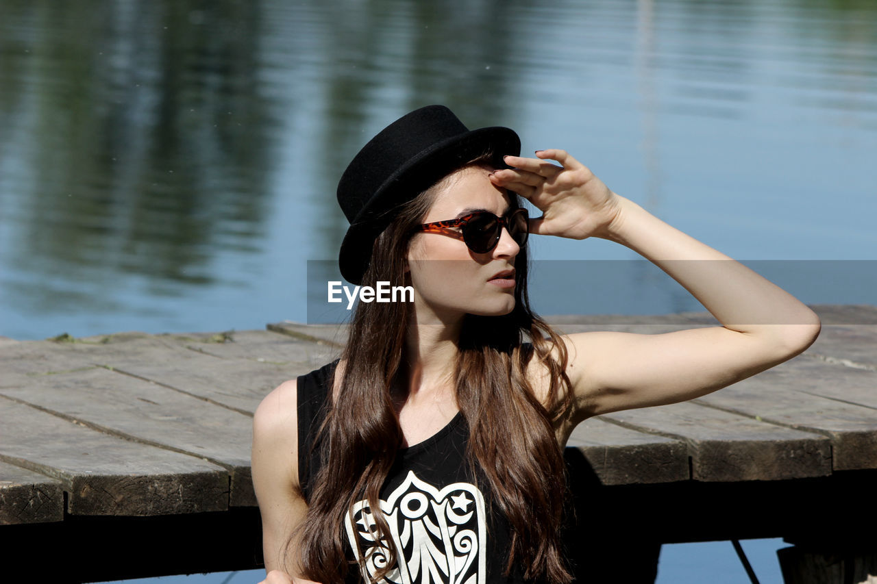 Young woman in sunglasses looking away while standing by lake
