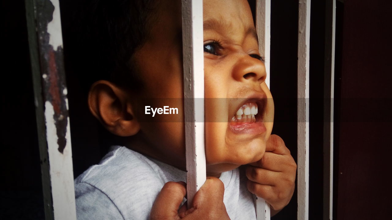 Close-up of aggressive boy holding security bars of window