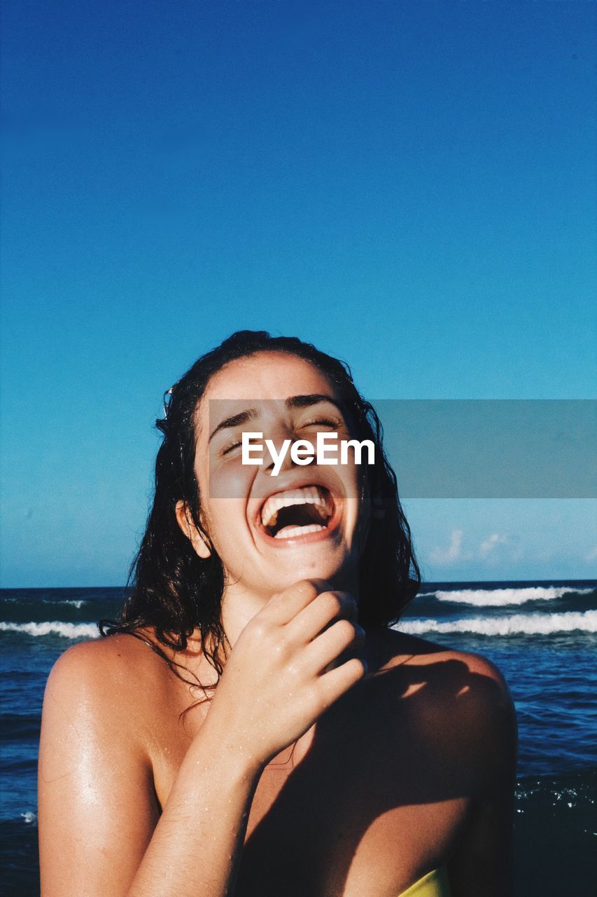 Happy young woman at beach against clear blue sky