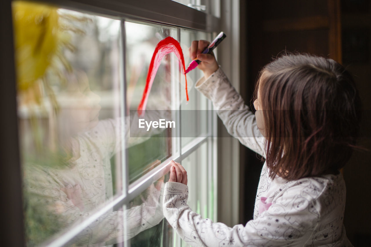 A small child draws a bright sun and rainbow on a window pane