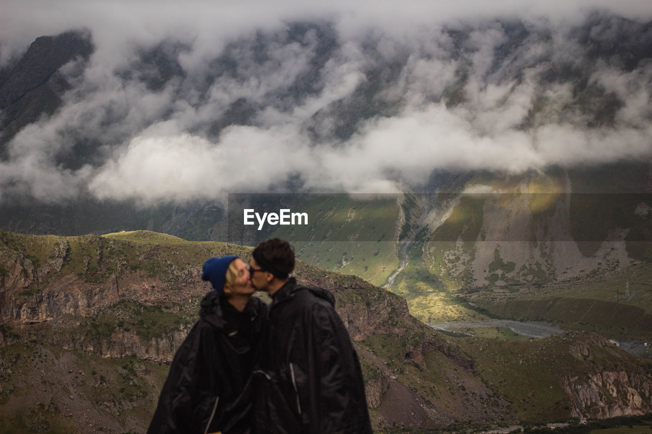 People kissing on mountain against sky during winter