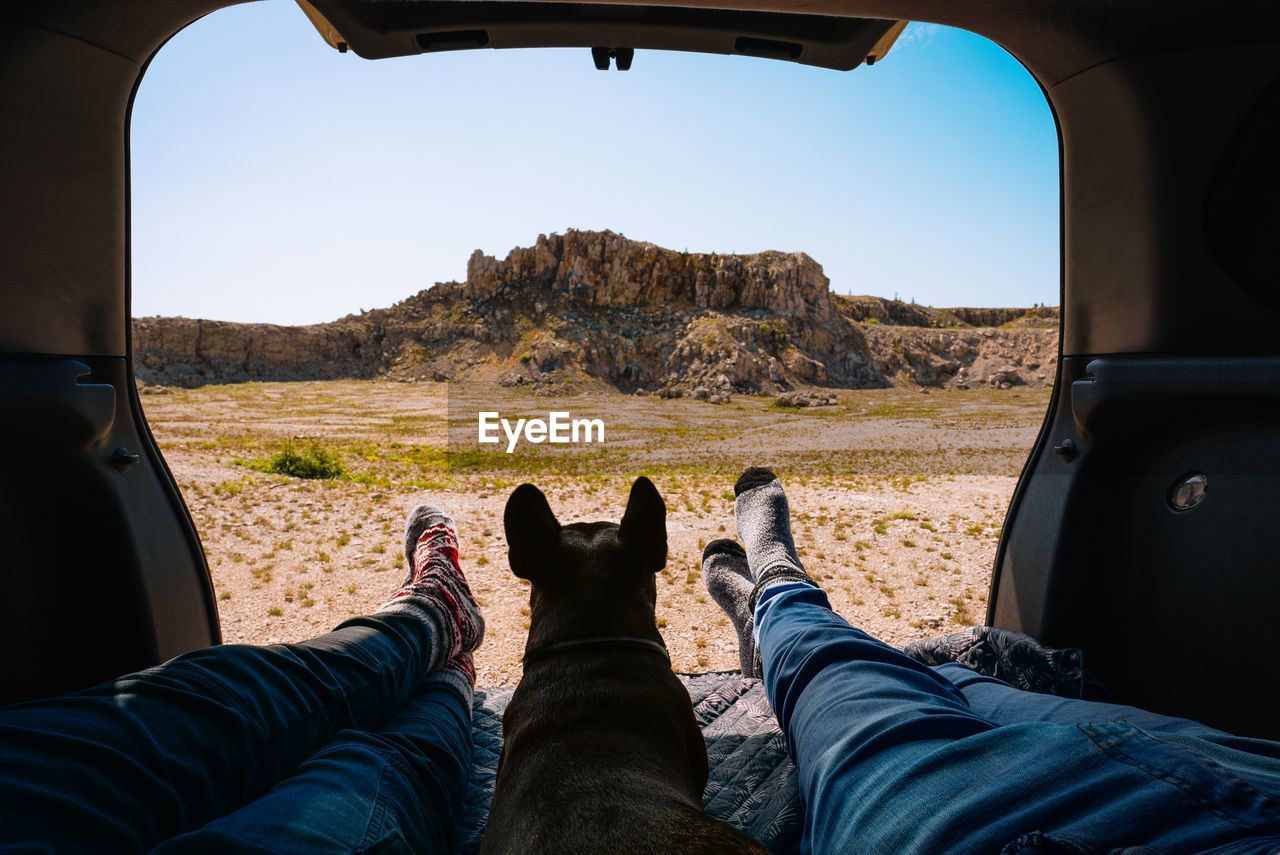 Low section of man and woman sitting in car trunk with french bulldog dog against mountains. travel. 