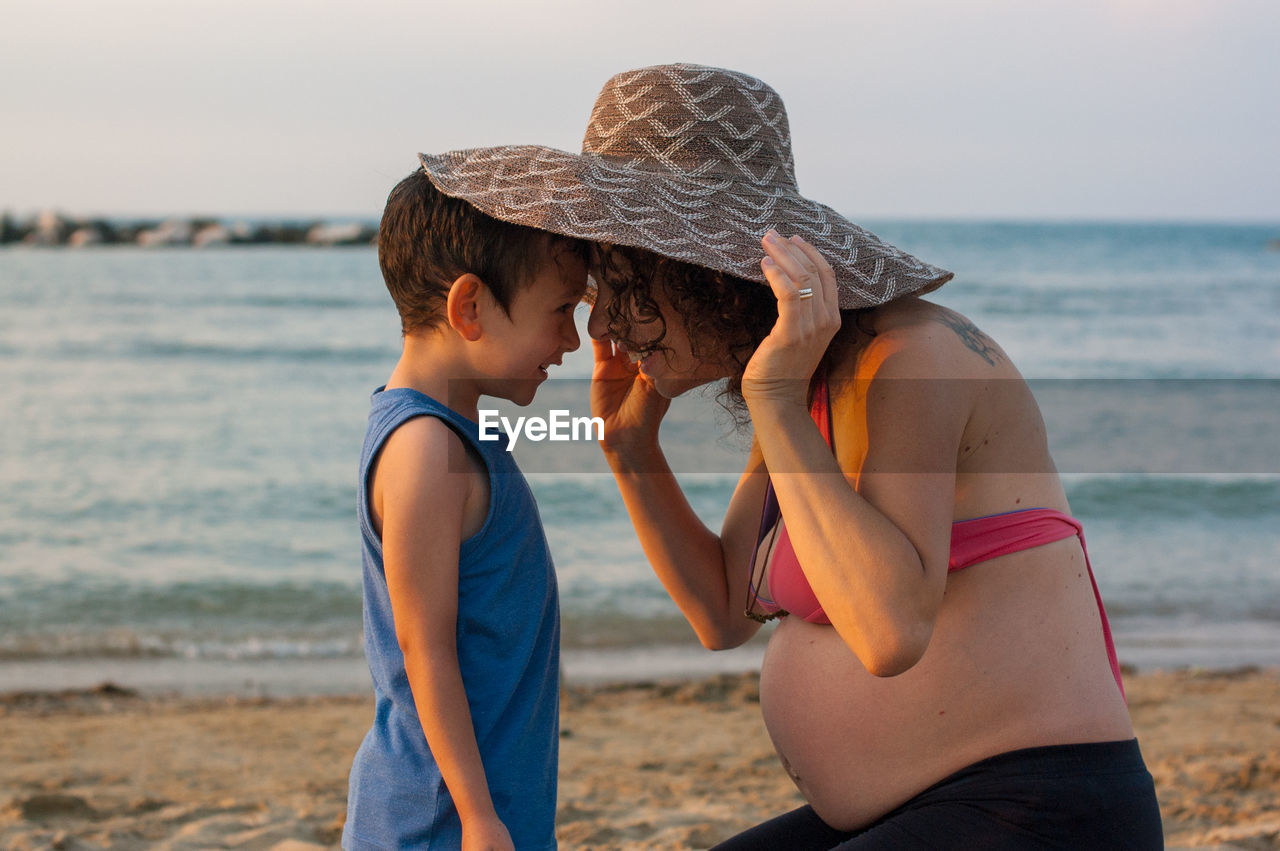 Smiling pregnant mother and son against sea at beach