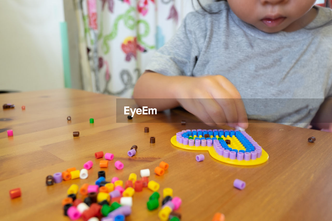 Midsection of girl playing with beads on table at home