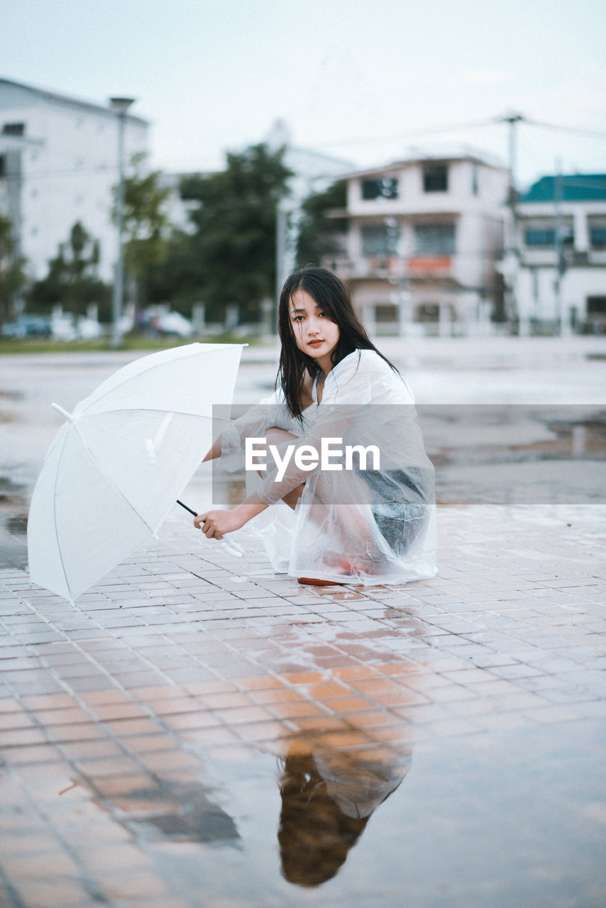 Portrait of young woman with umbrella sitting outdoors