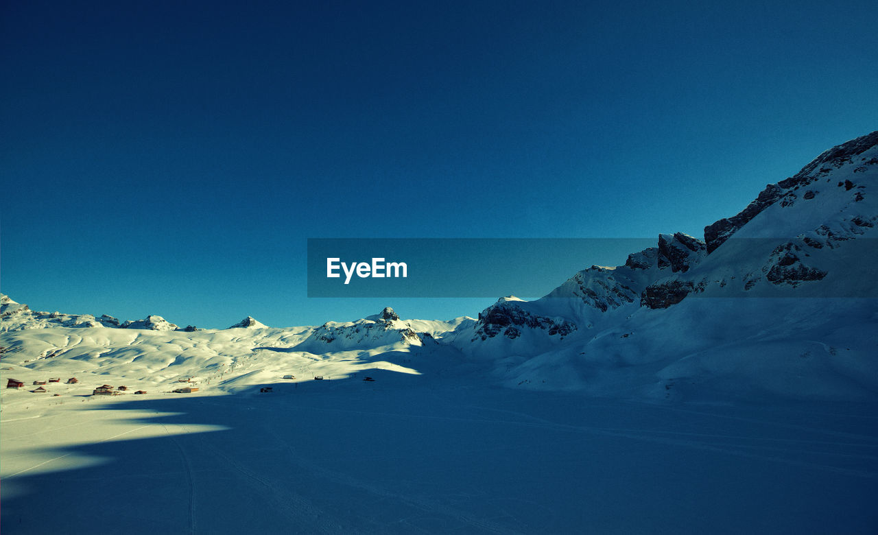 Scenic view of snow covered mountains against clear blue sky