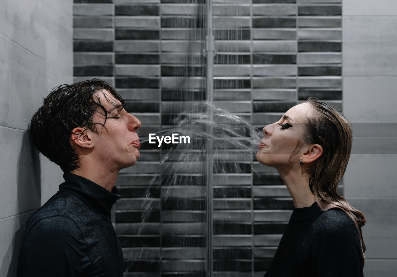 Young couple spitting water at each other in shower