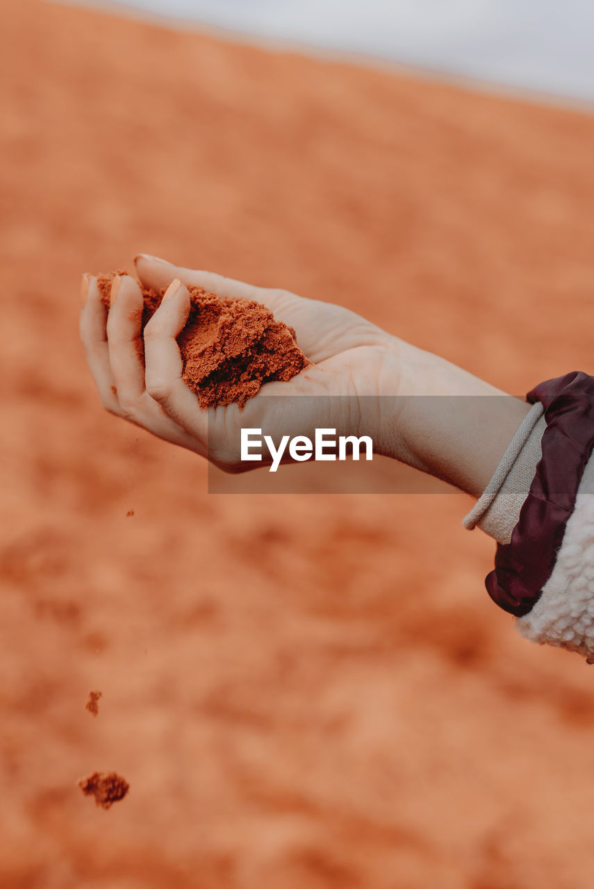 Unrecognizable crop person with handful of red sand standing in wadi rum dry valley in jordan