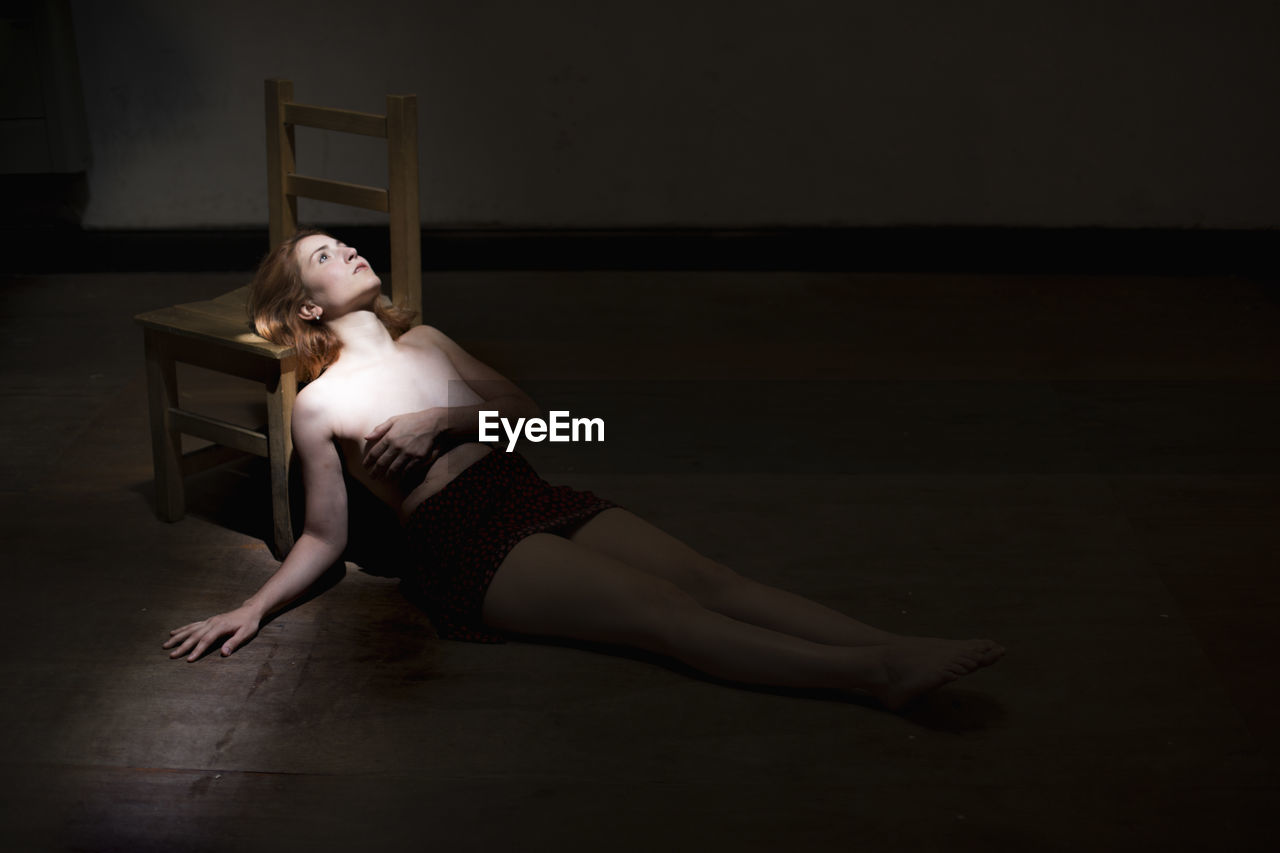 Thoughtful shirtless woman lying down in darkroom