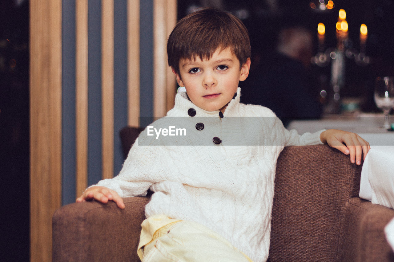 Portrait of cute boy sitting on sofa at home