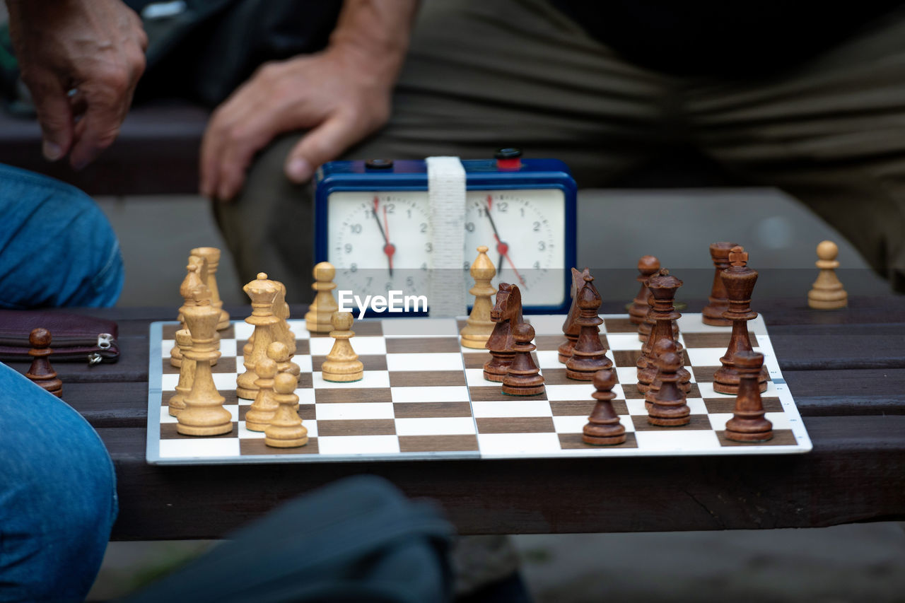 Midsection of men playing chess by clock on table