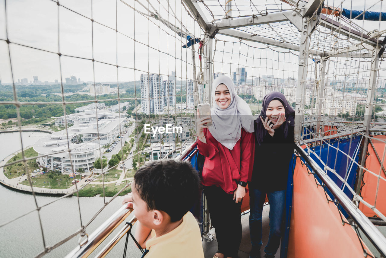 Sisters with mobile phone looking at boy while standing on covered footbridge