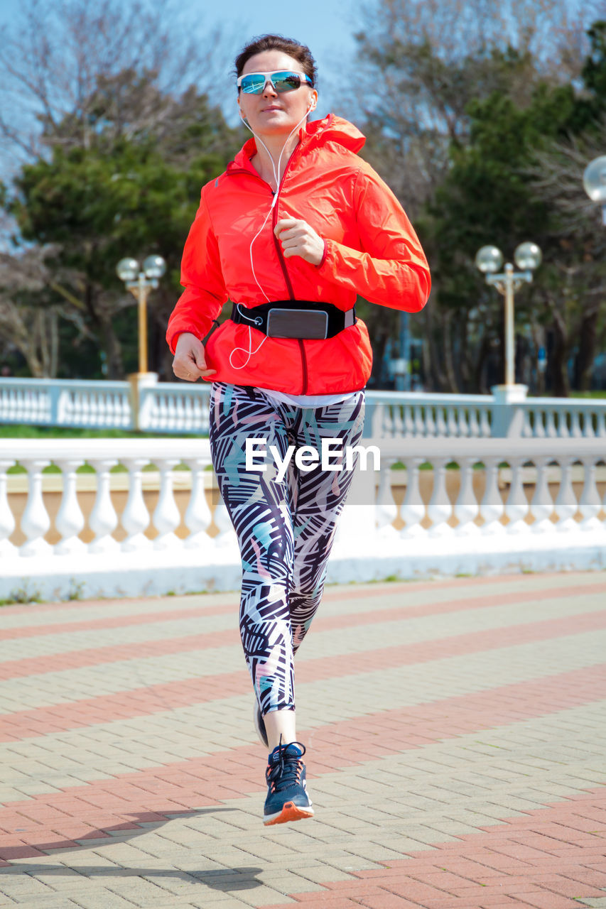 A full-length athletic woman in bright clothes is jogging in the morning around the city
