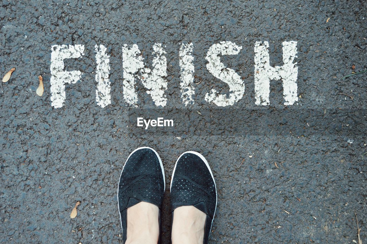 Low section of woman standing by finish text on road