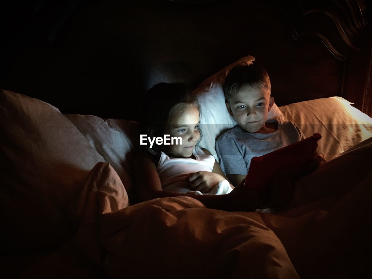 Smiling siblings using digital tablet on bed at home