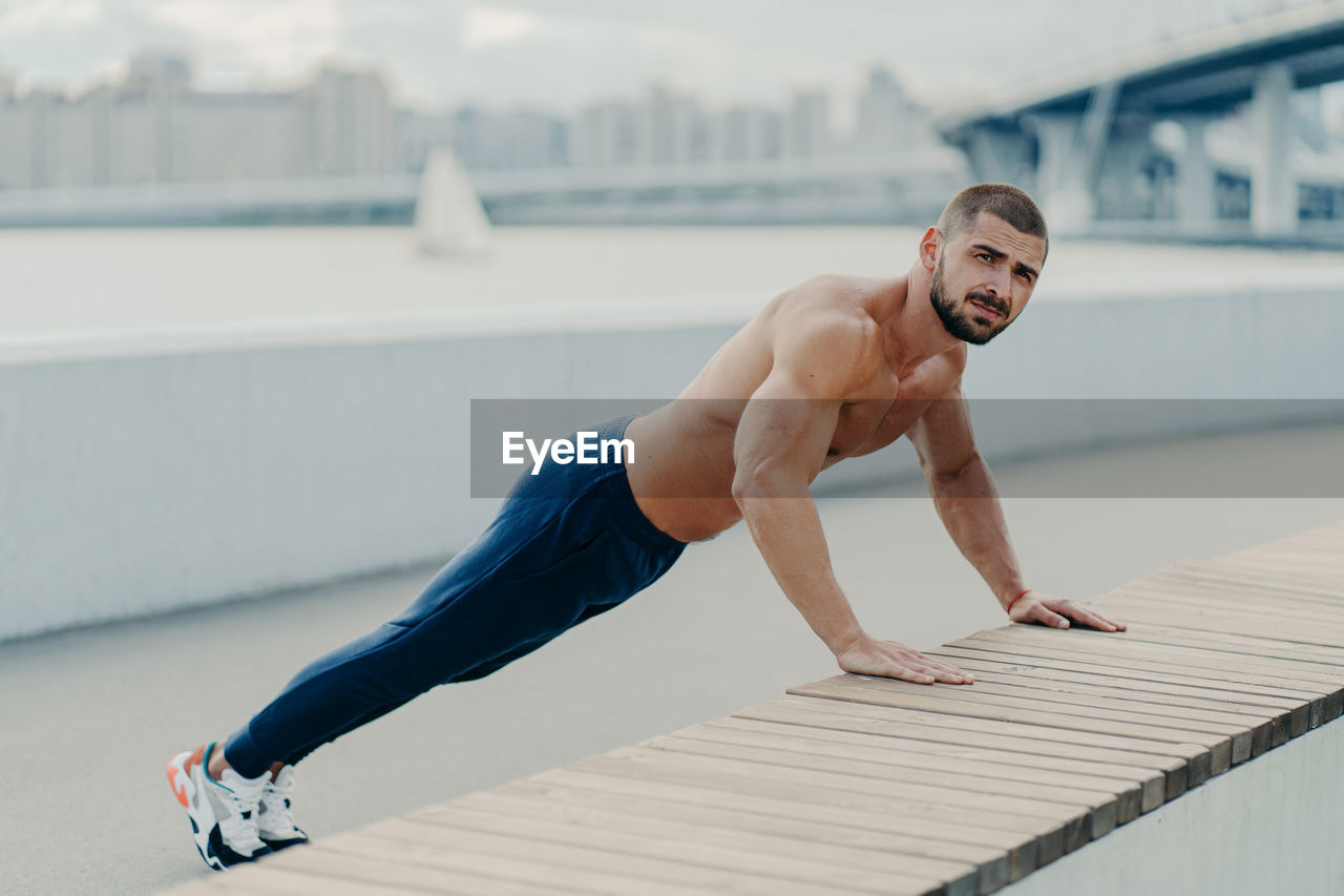 FULL LENGTH OF SHIRTLESS MAN CLIMBING OUTDOORS