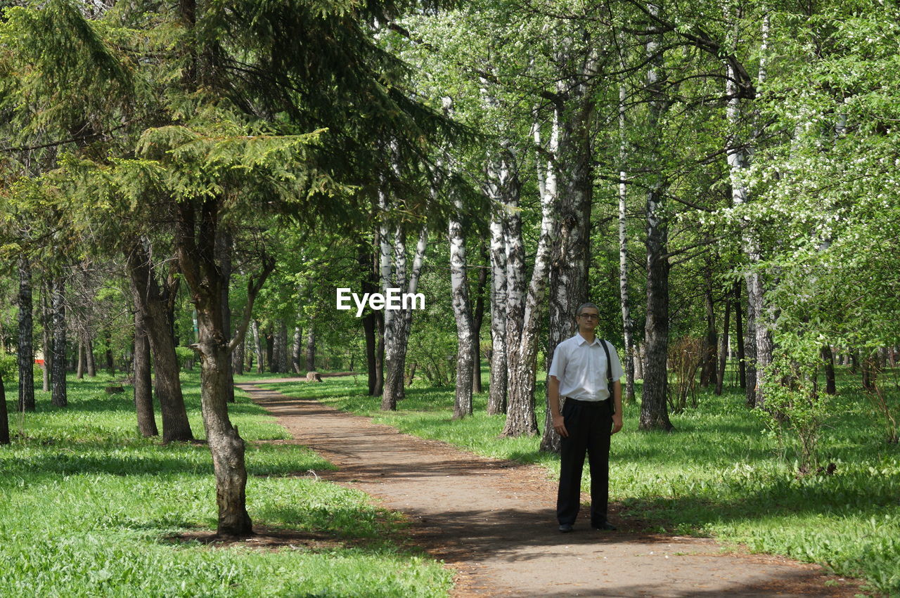 Full length of man standing on road at forest during sunny day