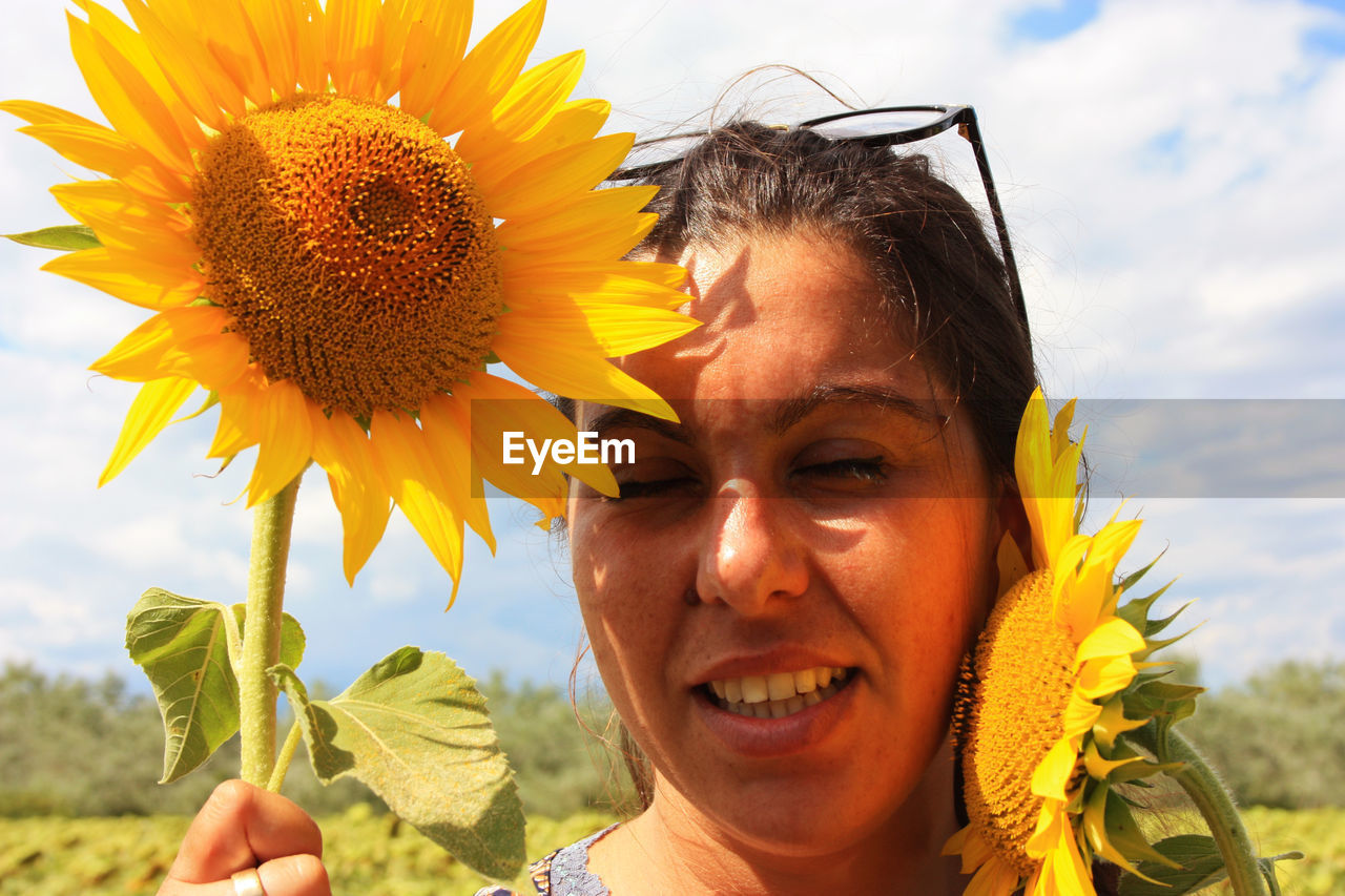 CLOSE-UP PORTRAIT OF A SMILING YOUNG WOMAN WITH SUNFLOWER
