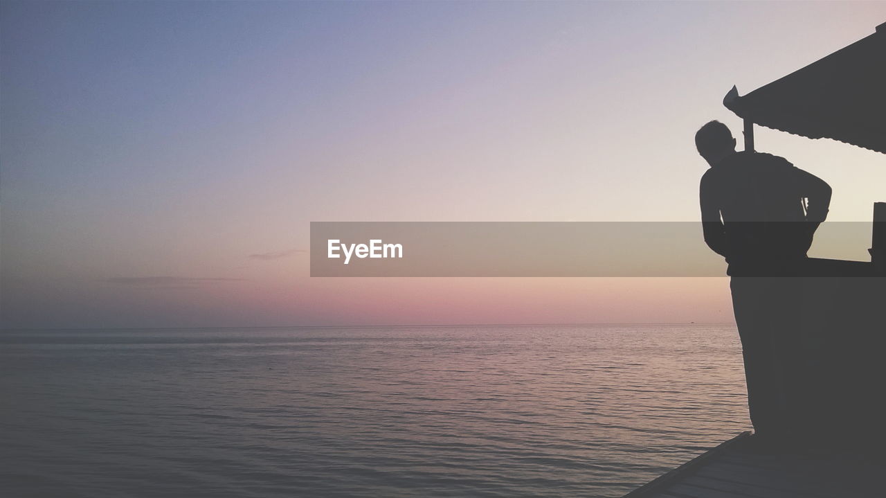 Silhouette man in boat on sea against clear sky during sunset