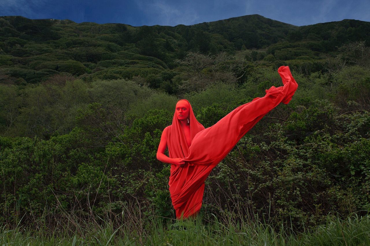 YOUNG WOMAN WITH RED UMBRELLA AGAINST MOUNTAIN