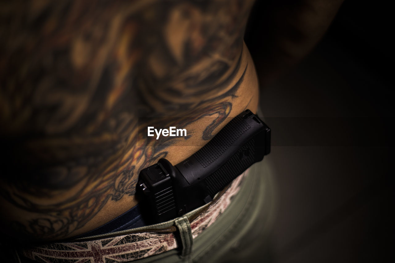 Midsection of tattooed man with gun in darkroom