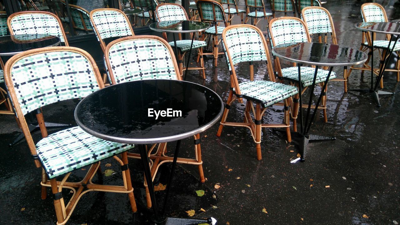 Empty chairs and tables arranged on wet sidewalk cafe