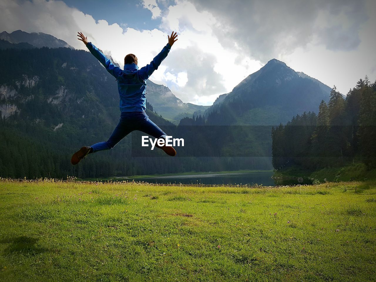 Rear view of man jumping on field against sky