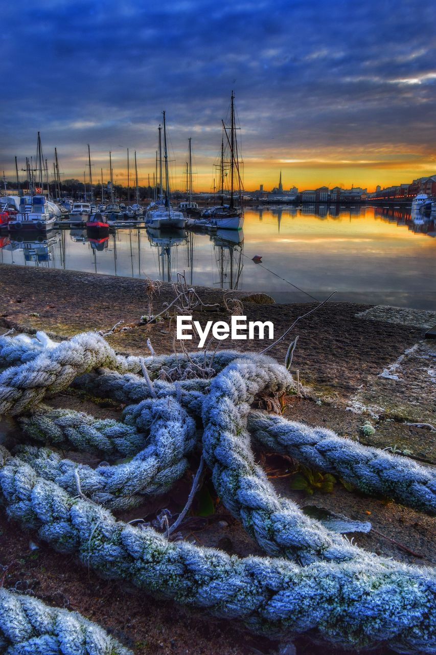 BOATS MOORED AT HARBOR AGAINST CLOUDY SKY