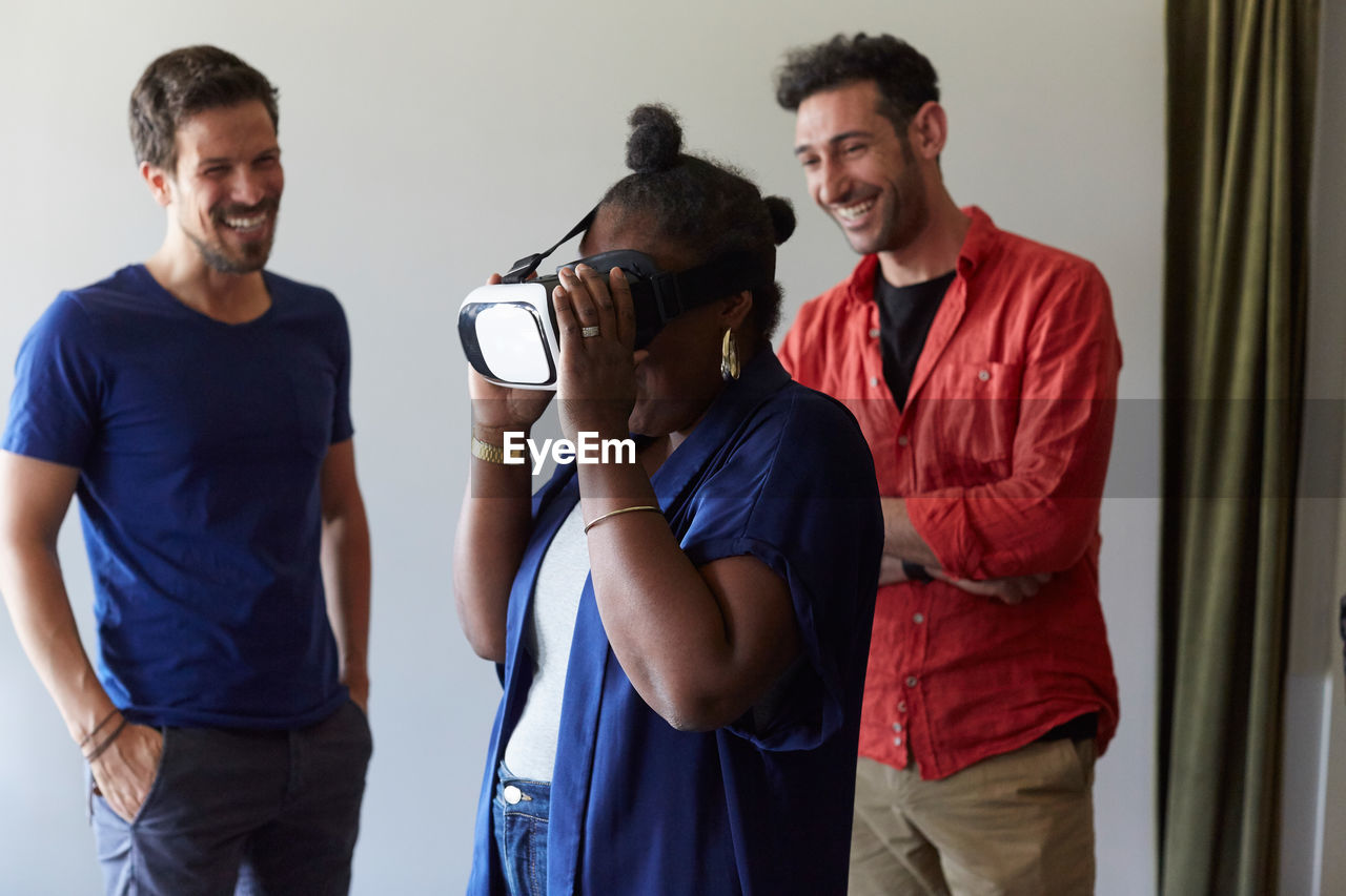 Businessmen smiling while looking at female colleague using virtual reality simulator in office