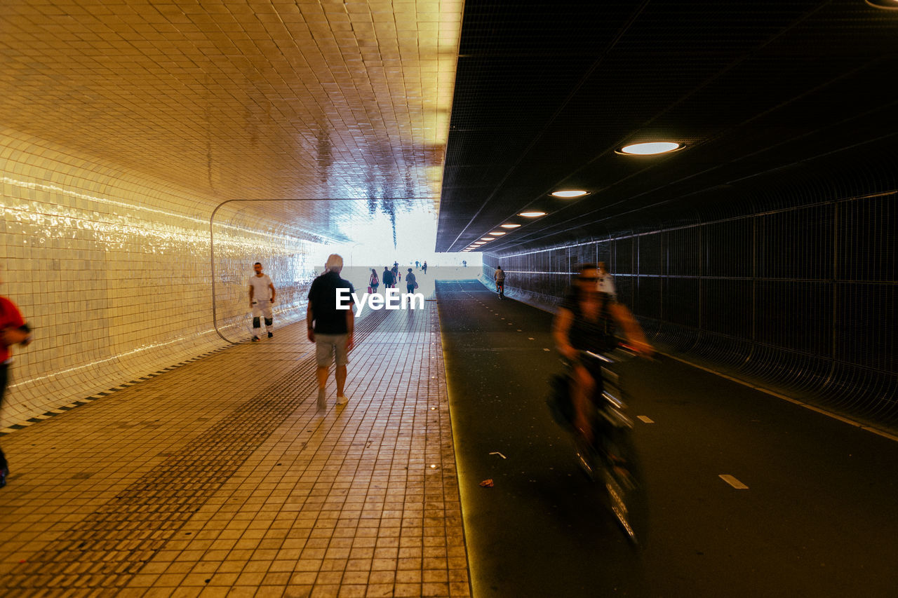 PEOPLE WALKING IN ILLUMINATED TUNNEL