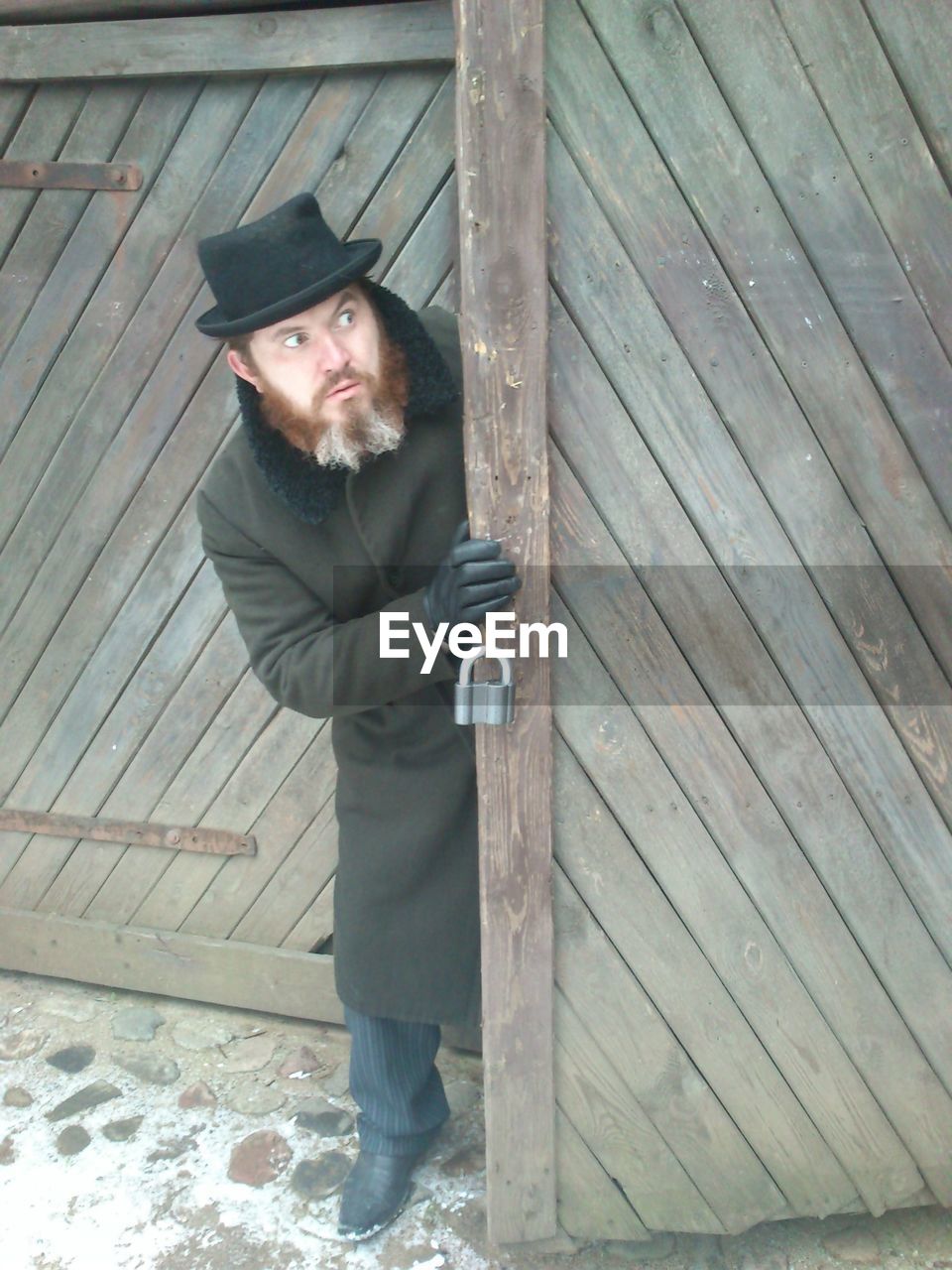 Full length of bearded man looking away while standing by wooden door