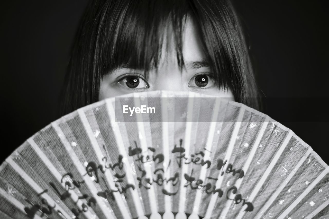 Portrait of young woman holding hand fan against black background