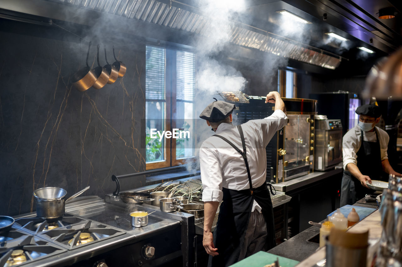 Chefs wearing protective face mask cooking dish in restaurant kitchen