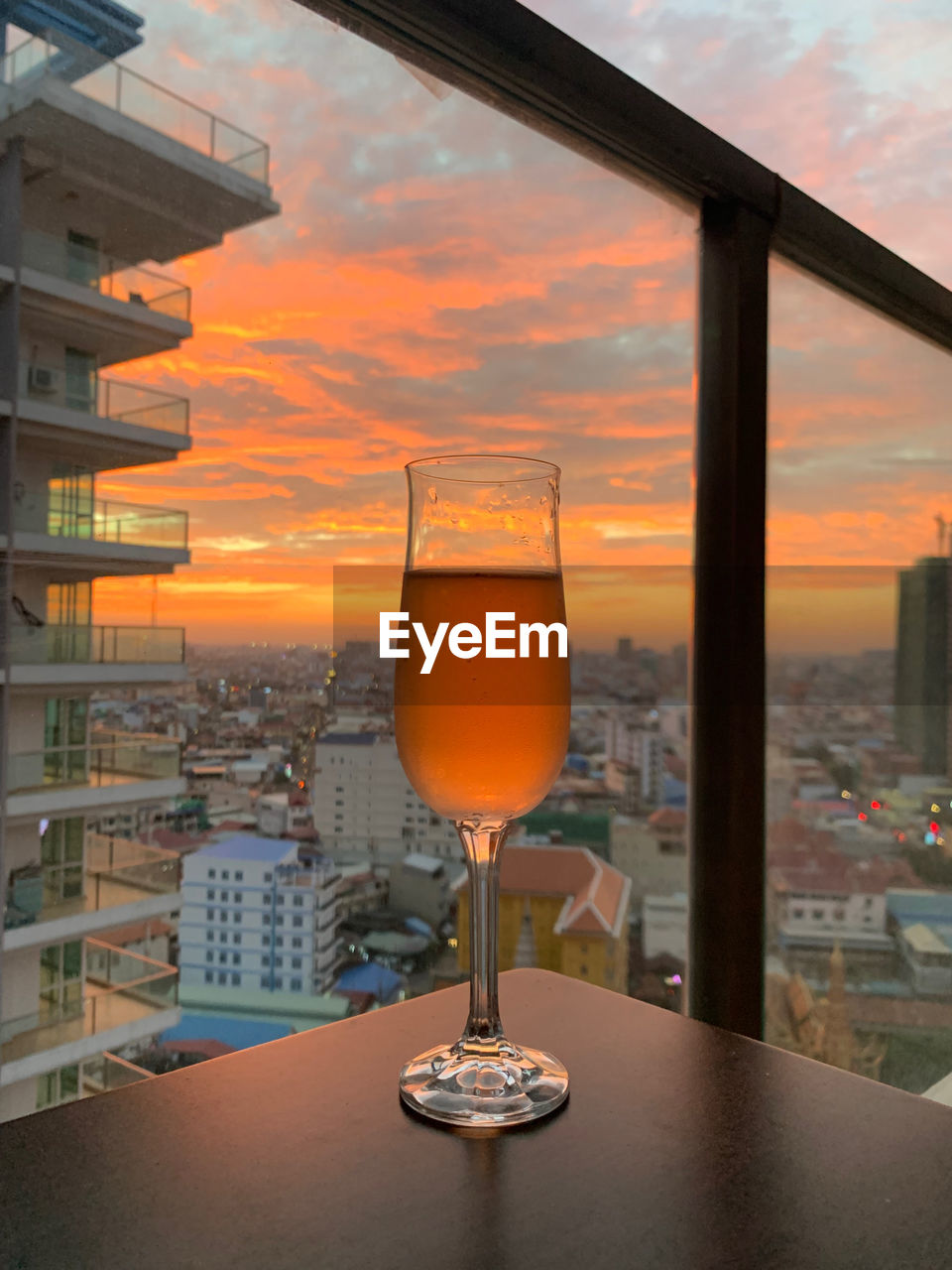 sunset, drink, alcohol, refreshment, food and drink, sky, glass, architecture, city, cloud, reflection, wine, nature, orange color, household equipment, drinking glass, built structure, building exterior, wine glass, no people, dusk, travel destinations, window, building, cityscape, travel, table, water, business, outdoors, restaurant, food, urban skyline, cocktail, balcony, scenics - nature, wealth, twilight, alcoholic beverage