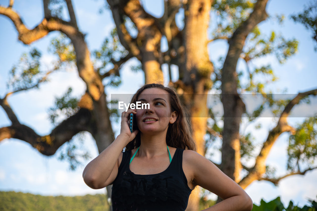 PORTRAIT OF HAPPY YOUNG WOMAN STANDING ON TREE