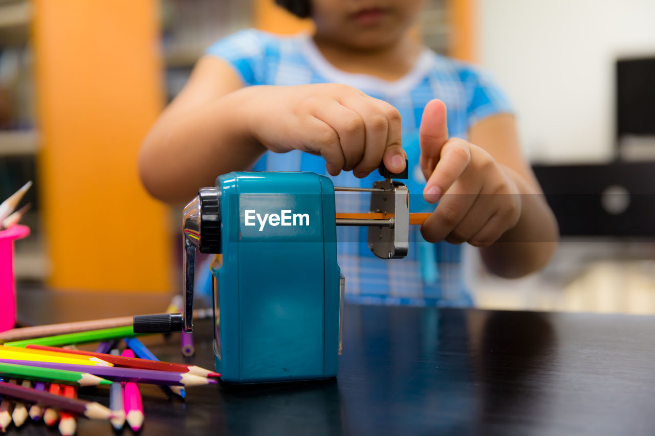 Midsection of girl sharpening pencil with equipment on table