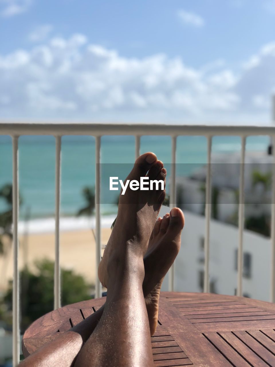 Low section of person resting on table by railing against sea and sky