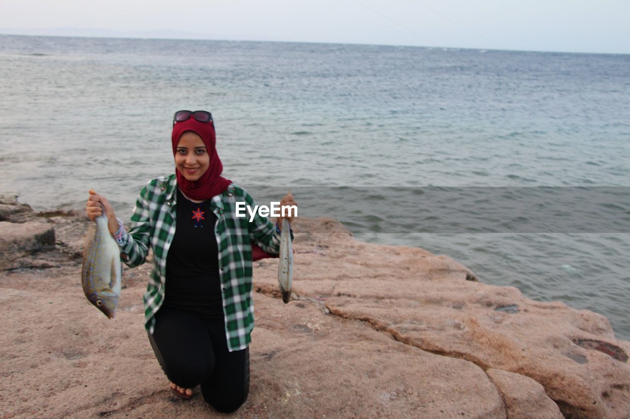 Portrait of smiling woman holding fish at beach