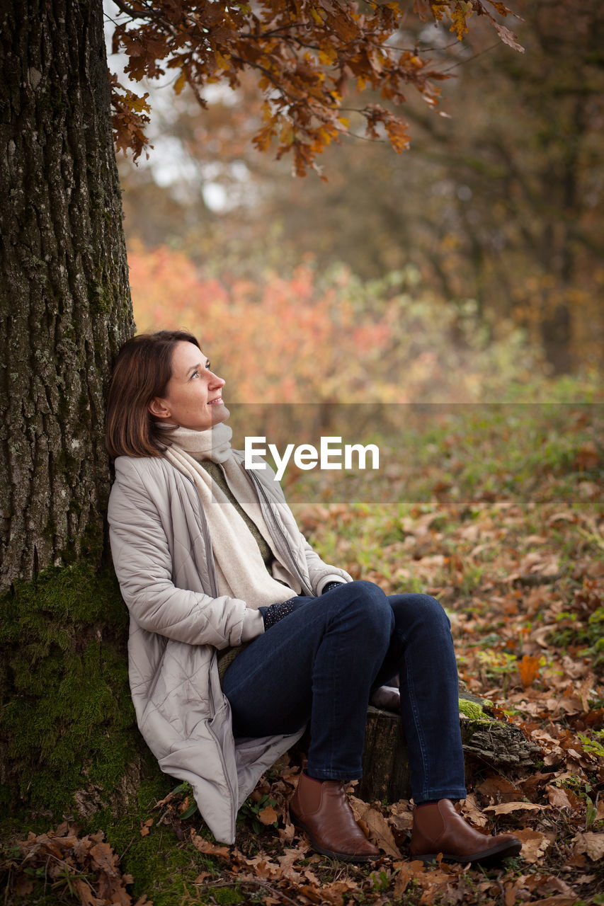 Young woman looking away while sitting on tree trunk